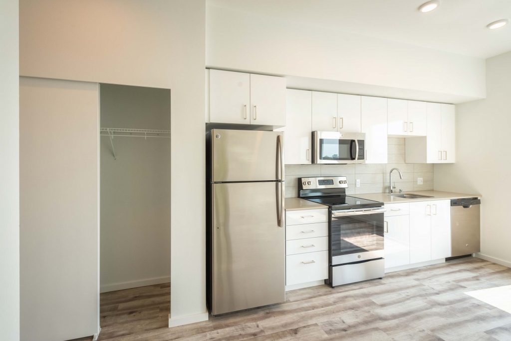 Unfurnished kitchen with empty closet, single sink, steel appliances, and wood-style flooring