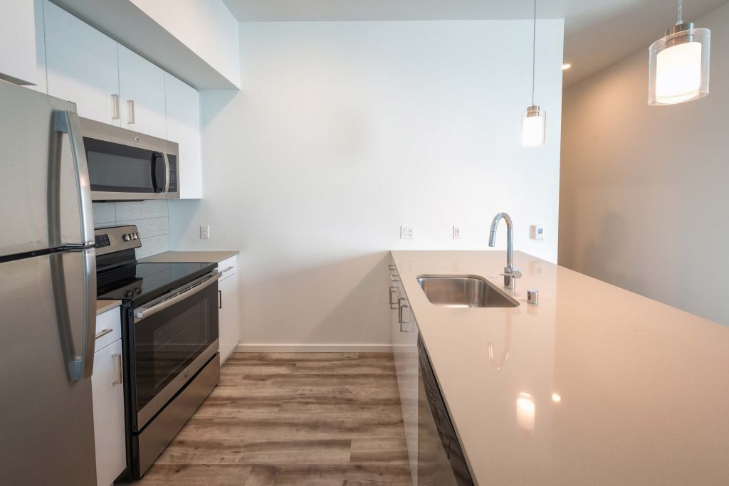 Unfurnished kitchen with single sink, steel appliances, designer lighting, and wood-style flooring