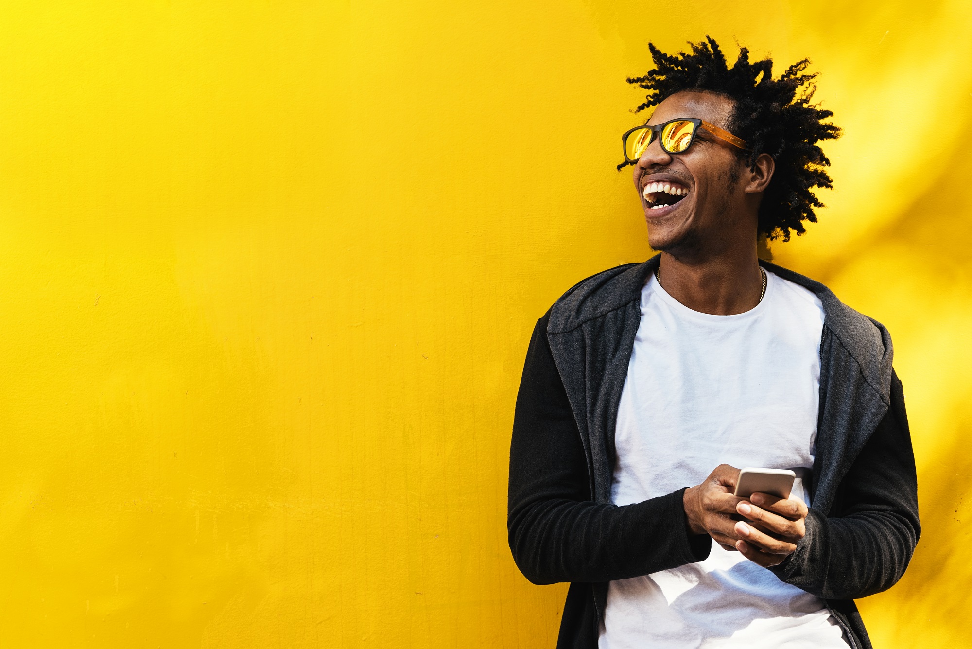 Man laughing while holding phone in front of yellow wall